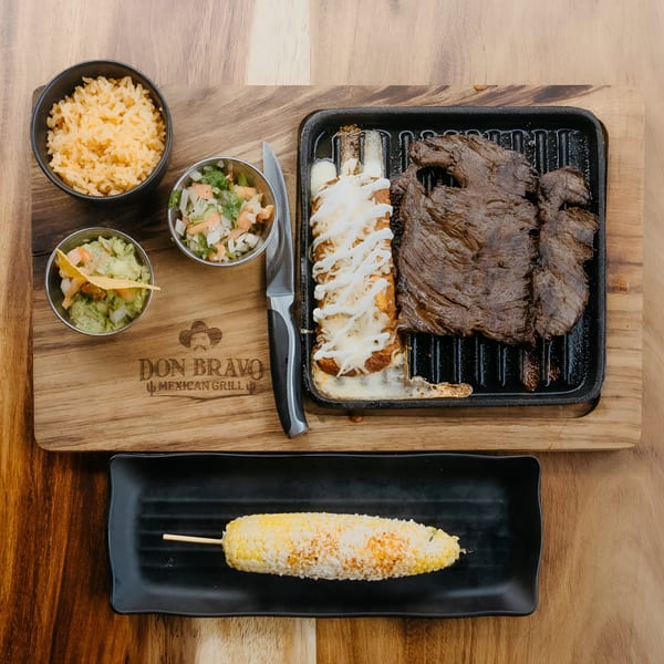 Don Bravo Mexican Grill's carne asada, enchiladas, rice, guacamole, salsa, and elote on a wooden board.