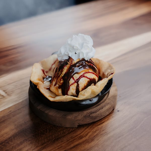 Fried ice cream dessert with chocolate and caramel drizzle, topped with whipped cream in a tortilla bowl.