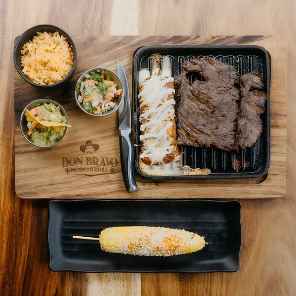 Don Bravo Mexican Grill's carne asada, enchiladas, rice, guacamole, salsa, and elote on a wooden board.