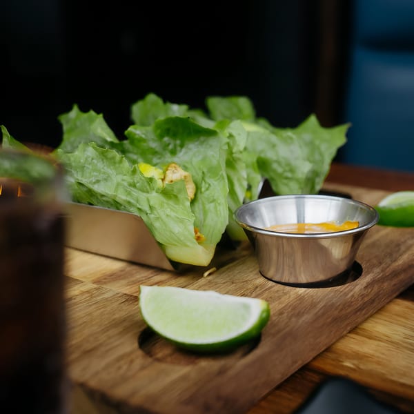 Lettuce wraps with chicken and avocado, served with a side of sauce and lime wedges.