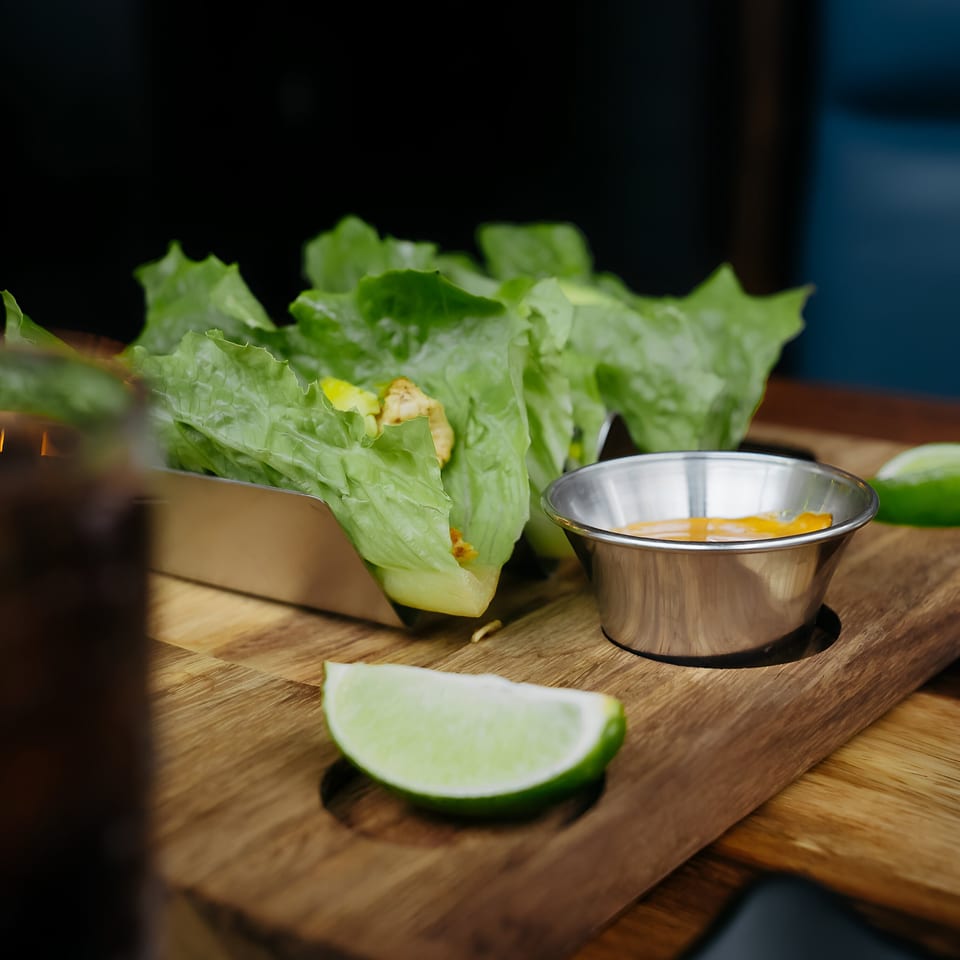 Lettuce wraps with chicken and avocado, served with a side of sauce and lime wedges.