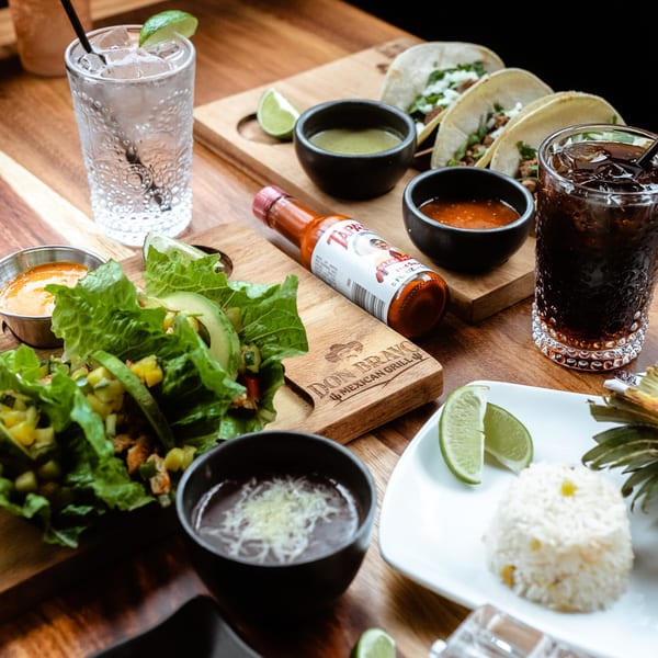 Don Bravo Mexican Grill spread with tacos, salad, rice, beans, drinks, and hot sauce on a wooden table.