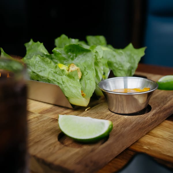 Lettuce wraps with chicken and mango, served with sauce and lime wedges on a wooden board.