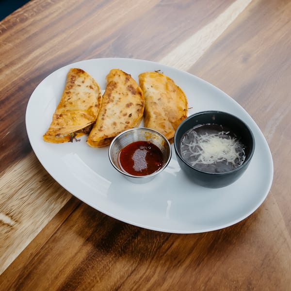 Three golden-brown quesadillas, a cup of red sauce, and a bowl of black bean soup with cheese.