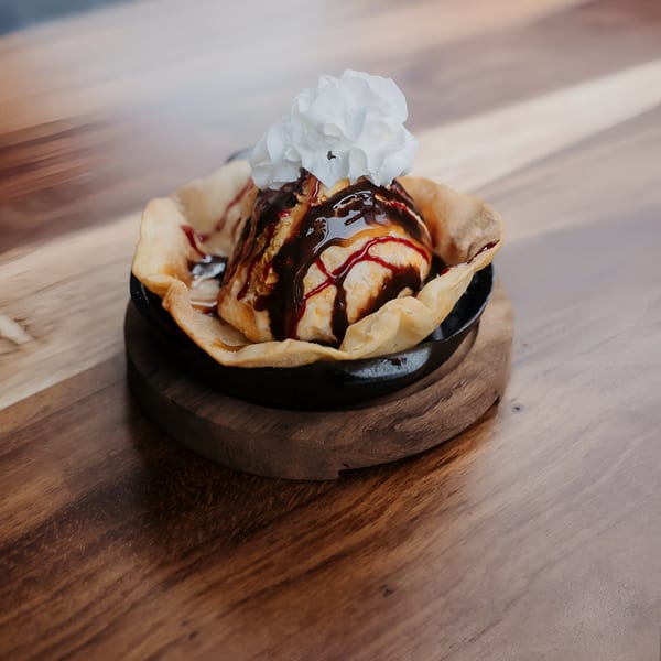 Fried ice cream dessert with chocolate and strawberry syrup, topped with whipped cream.