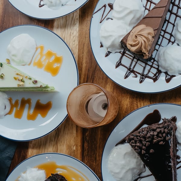 Overhead view of four dessert plates with various cakes, whipped cream, and sauces on a wooden table.
