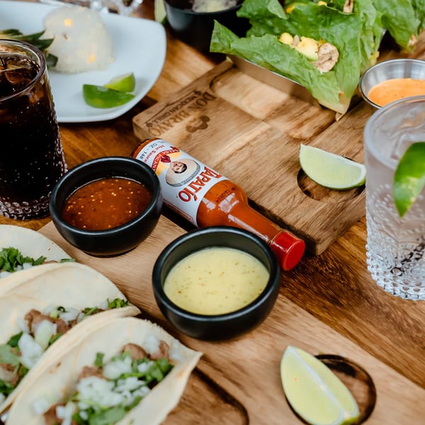 Don Bravo Mexican Grill tacos, sauces, and drinks on a wooden board.