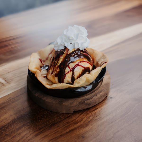 Fried ice cream dessert with chocolate and strawberry syrup, topped with whipped cream in a tortilla bowl.