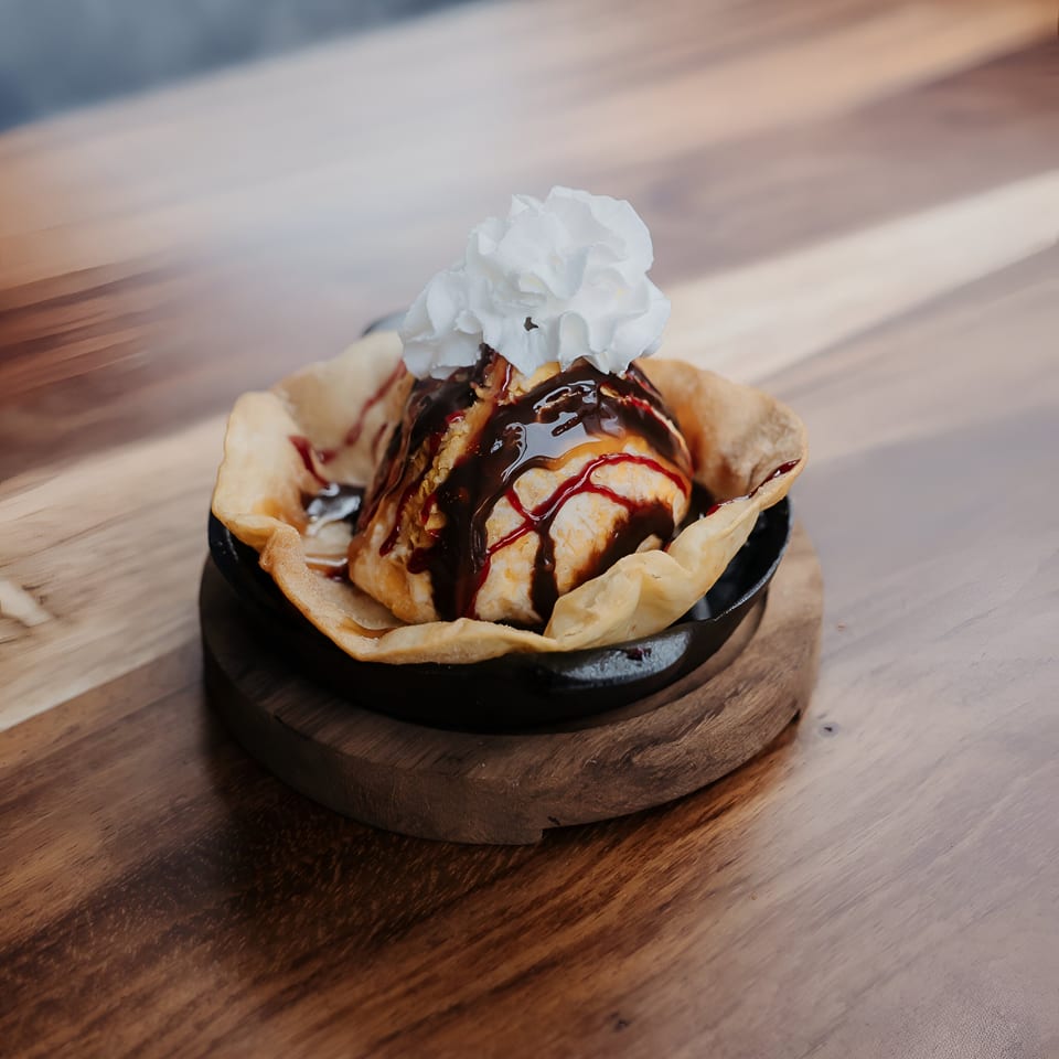 Fried ice cream dessert with chocolate and strawberry syrup, topped with whipped cream in a tortilla bowl.