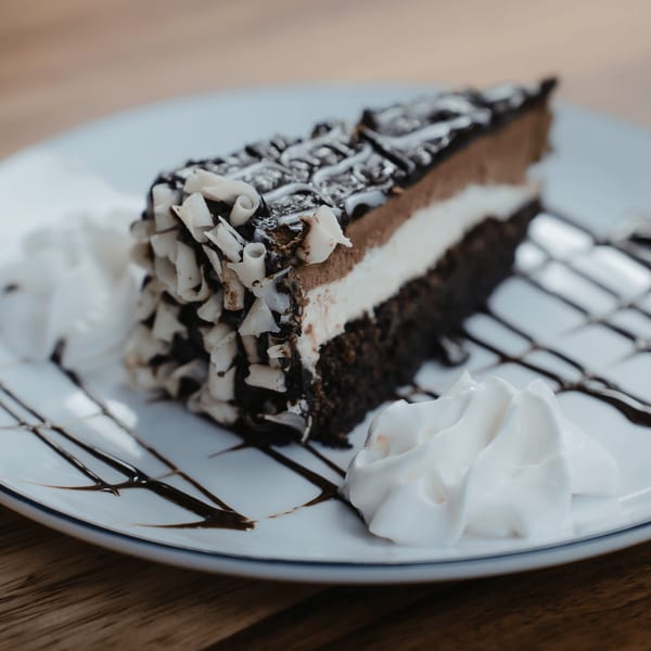 A slice of chocolate cake with white and milk chocolate layers, topped with chocolate shavings and whipped cream.
